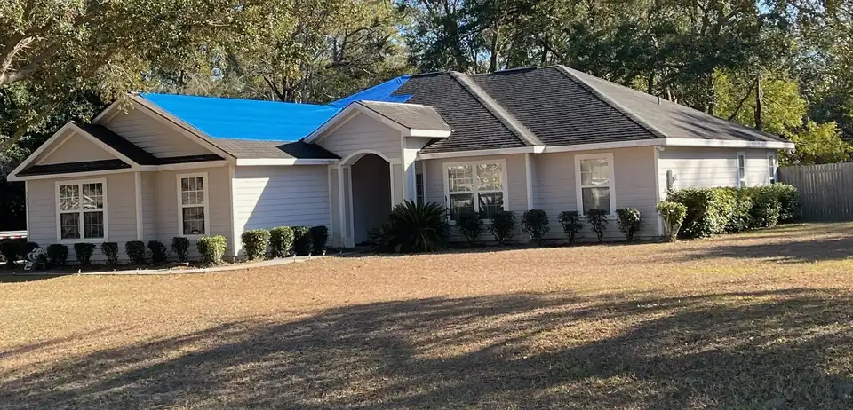 House with a blue emergency tarp over part of its shingle roof